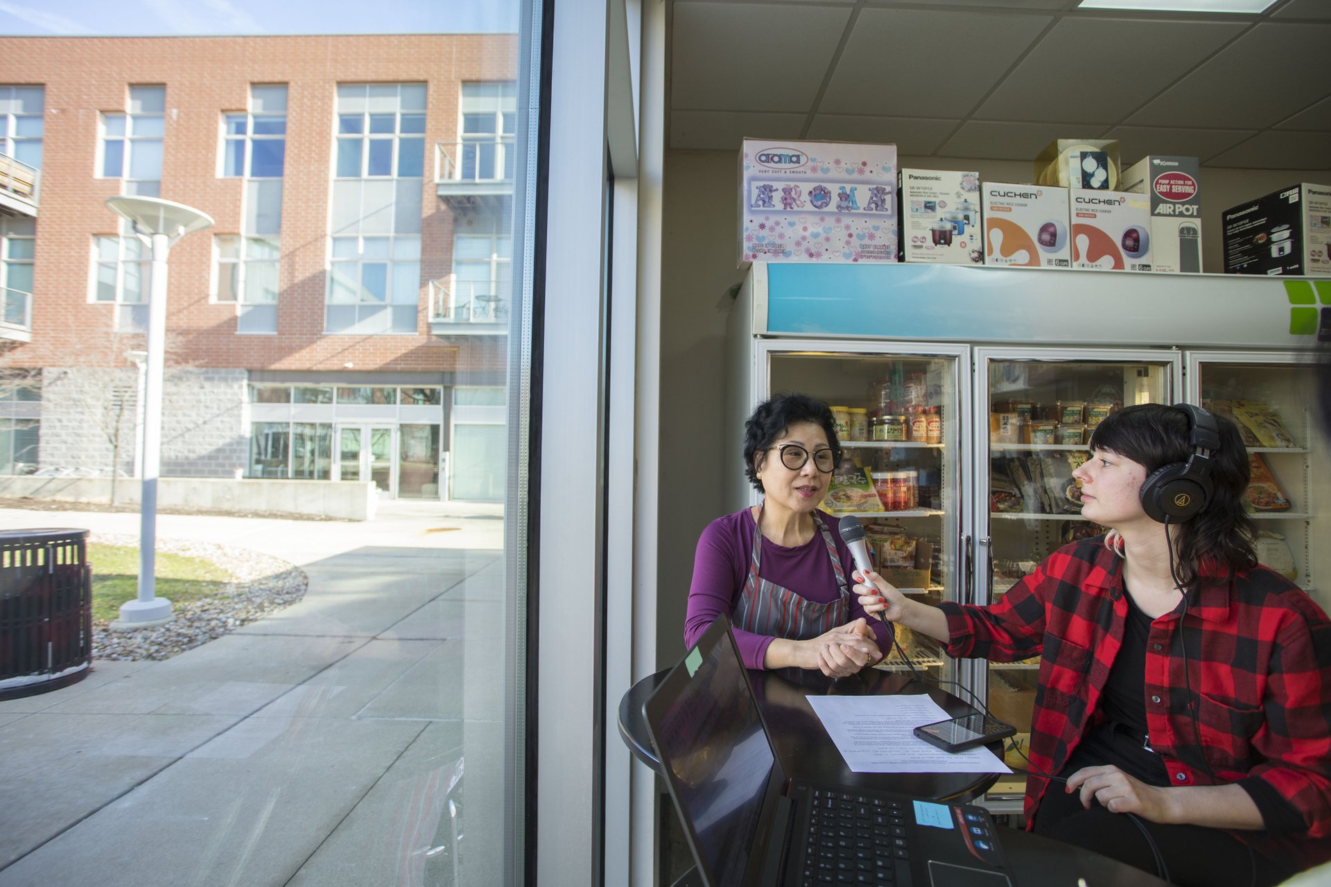 A woman speaks into a microphone being held by a student wearing headphones.