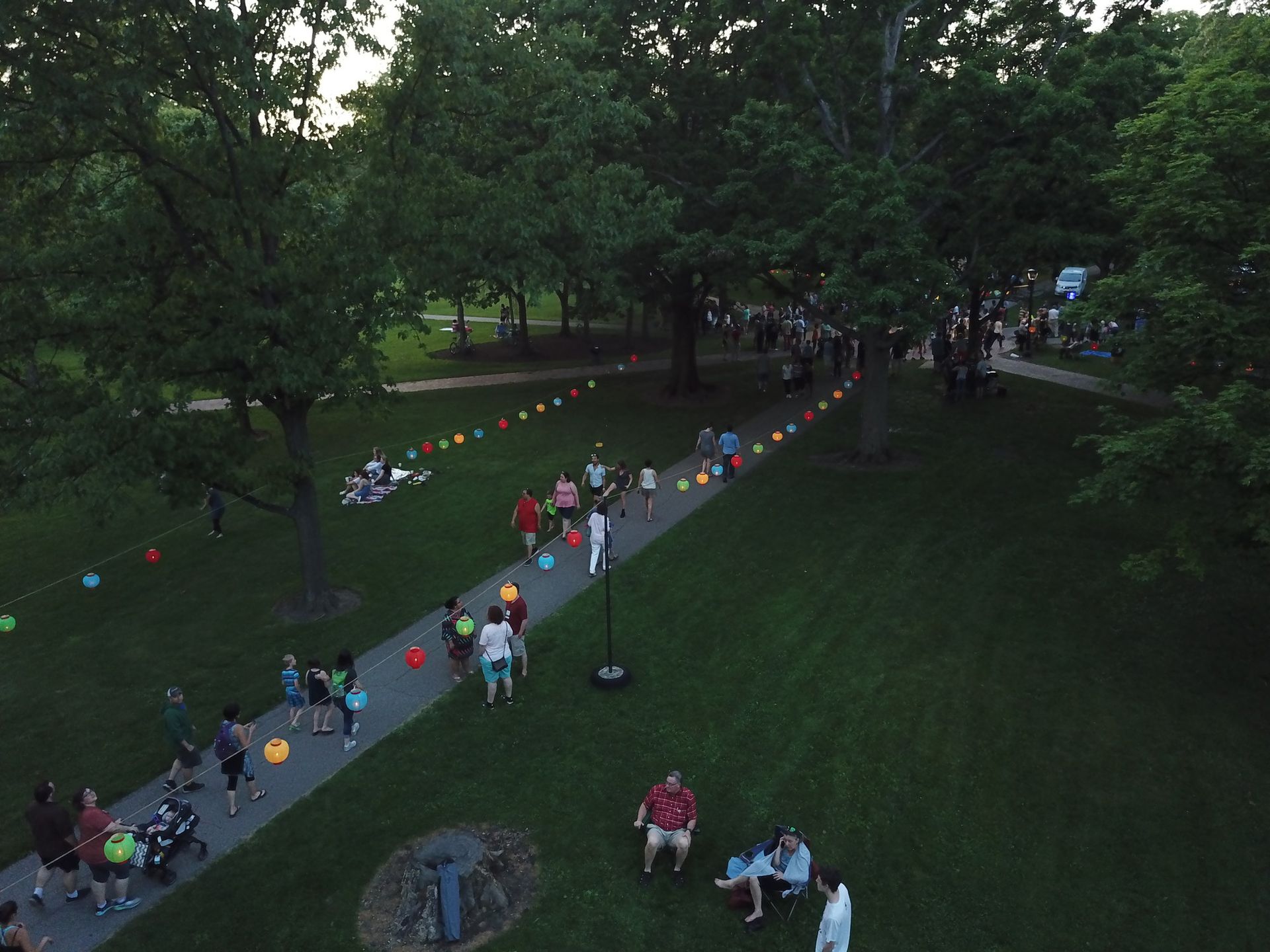 An overhead view of people walking down a path with hanging lanterns surrounding them.