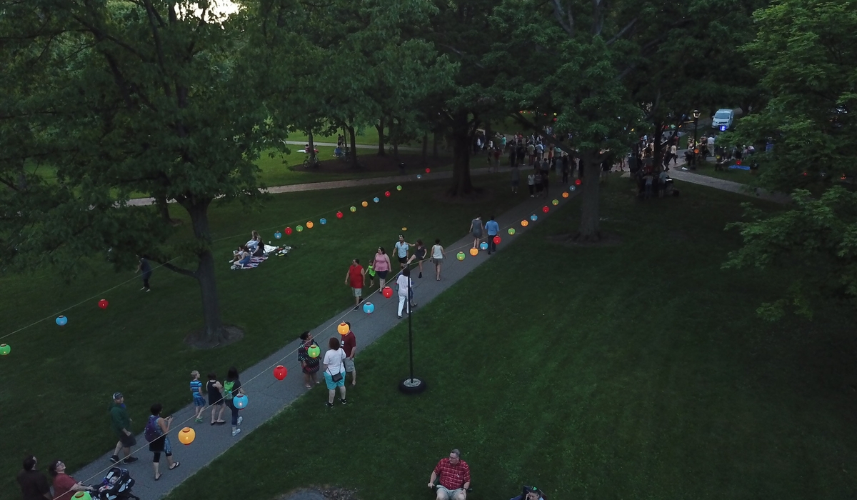 An overhead view of people walking down a path with hanging lanterns surrounding them.