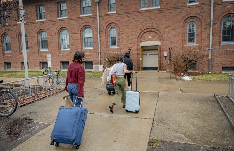 Three students wheel luggage into a building.