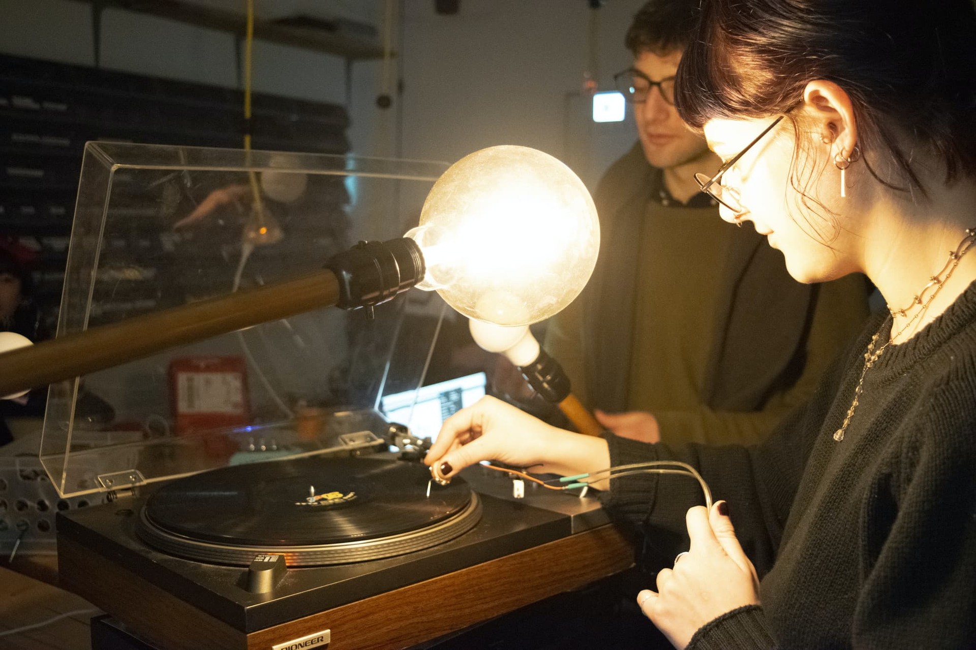 A student places a needle on a record with two large light bulbs in front of her.