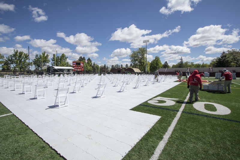 Workers lay large plastic squares down on a football field.