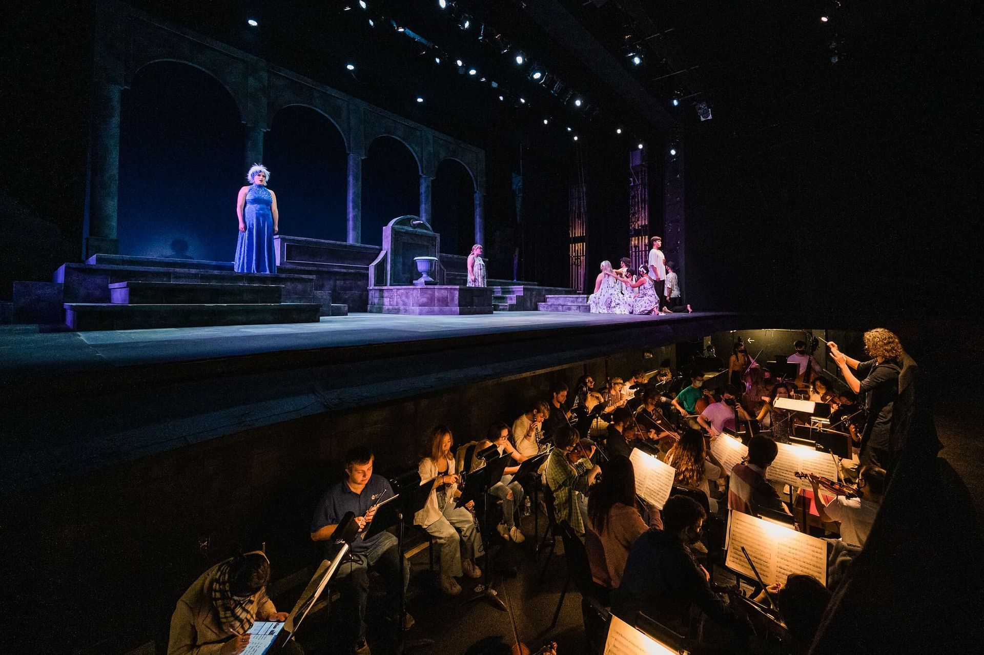 An orchestra plays in a pit while actors perform on stage.