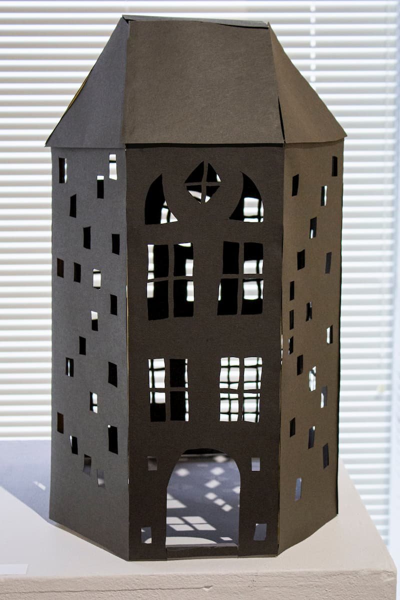Paper folded into a house with cut outs of windows.