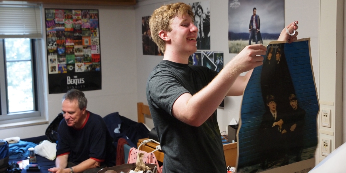 A student hangs a poster in his dorm room