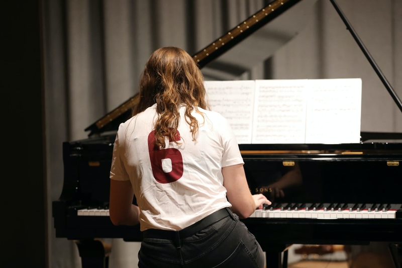 A woman wearing a sports jersey plays a piano.