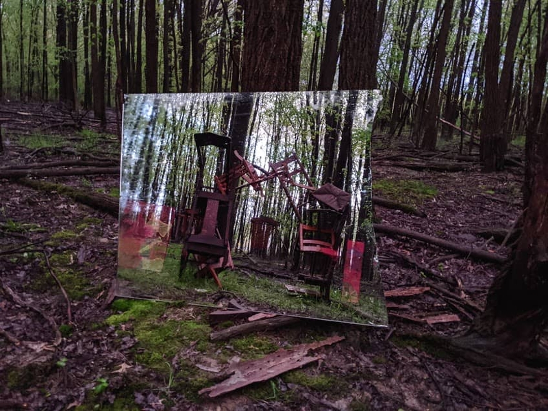 A large picture of chairs stacked on each other is leaned against a tree in a large field 