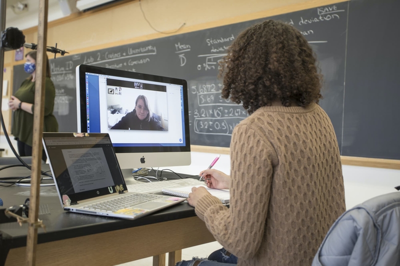 A student in a lab talks to her classmate on a computer monitor