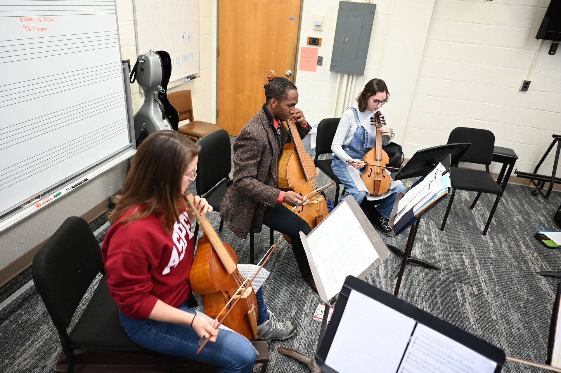 Three students practice de gamba in a practice room.