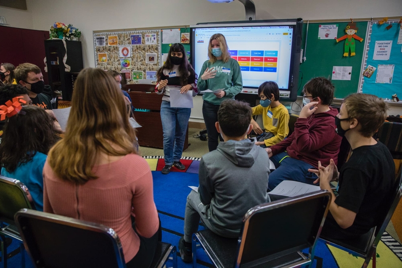 Two college students instruct grade school students in a classroom