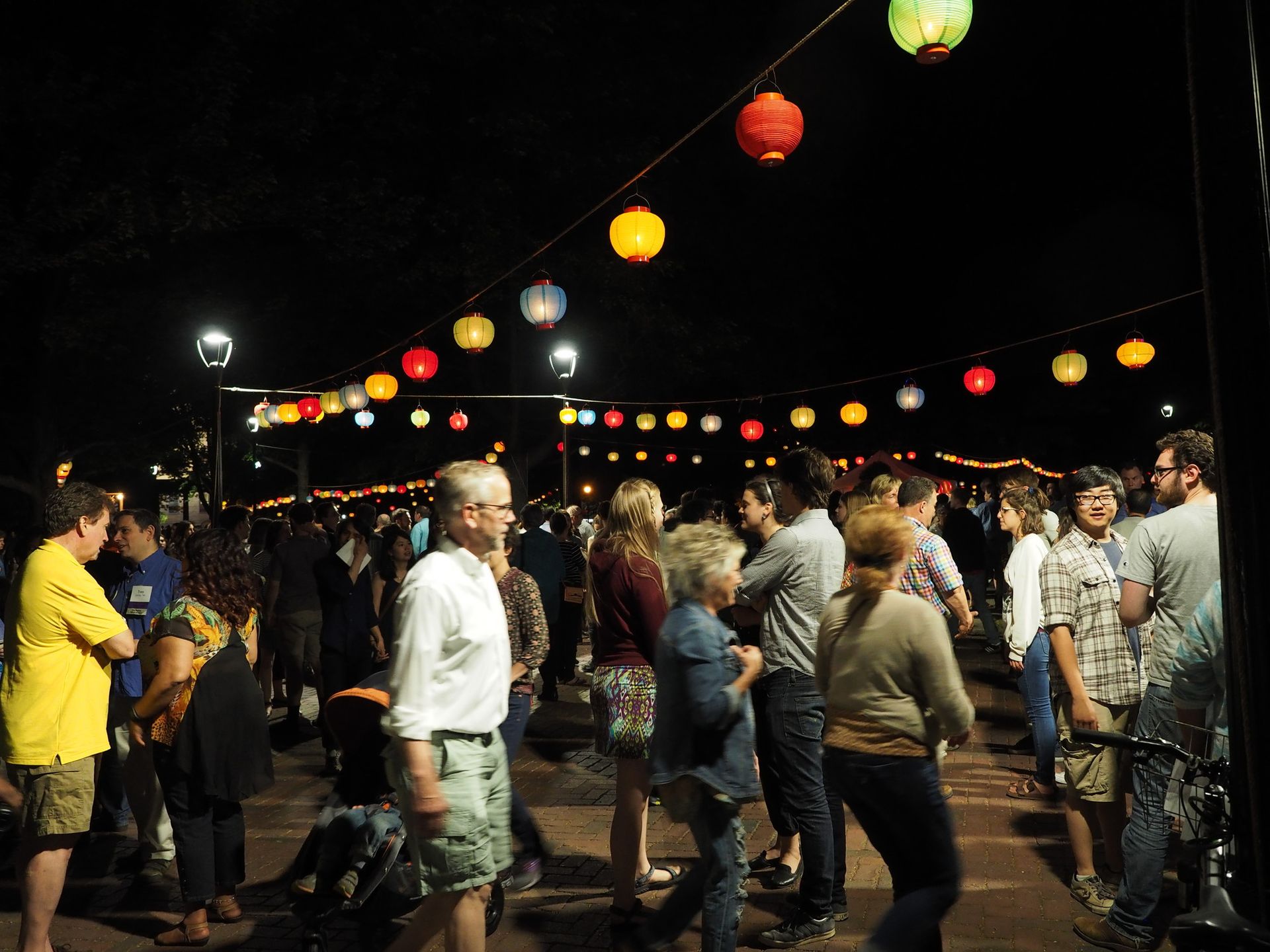 People walk quickly under hanging lanterns at night.