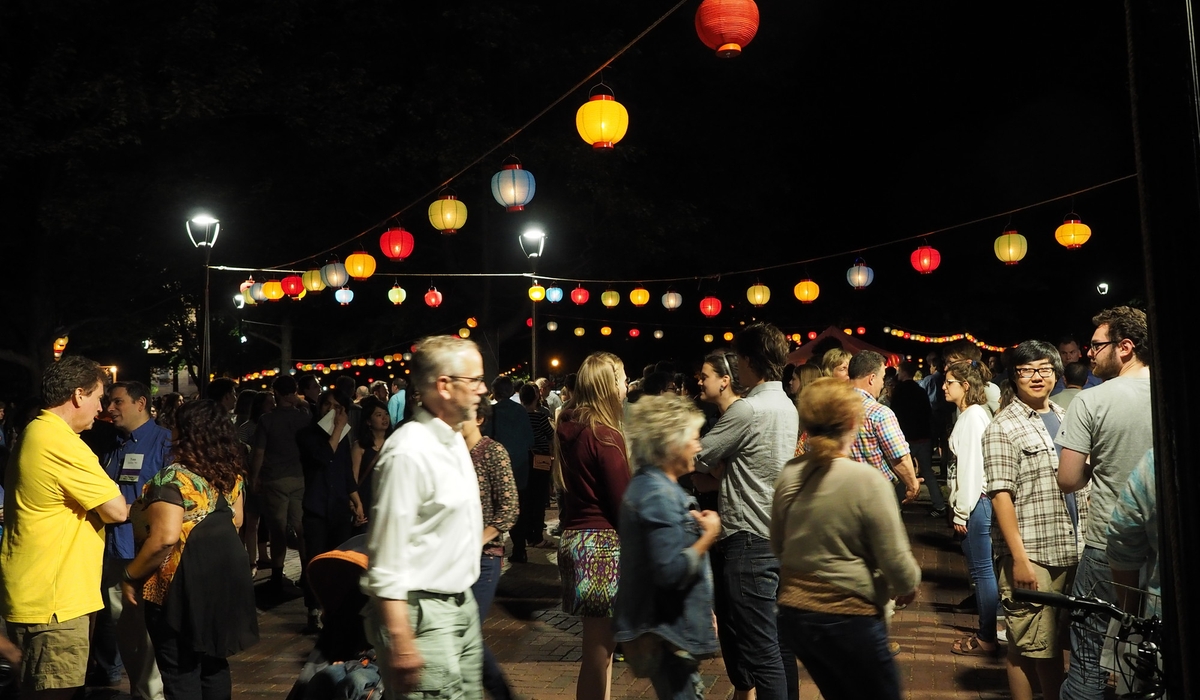 People walk quickly under hanging lanterns at night.