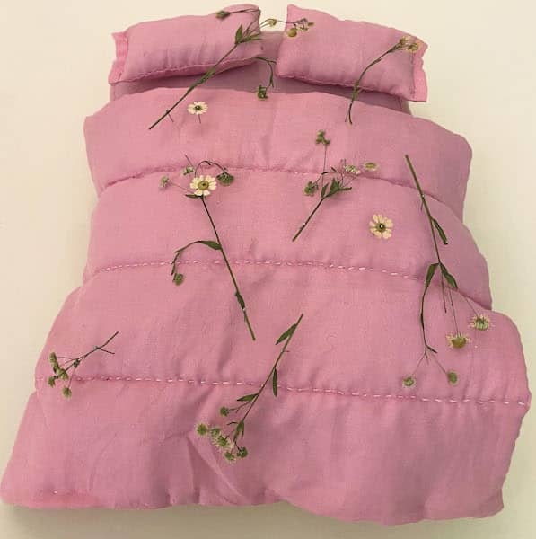 A hand stitched duvet and pillow with flowers strawn on top 