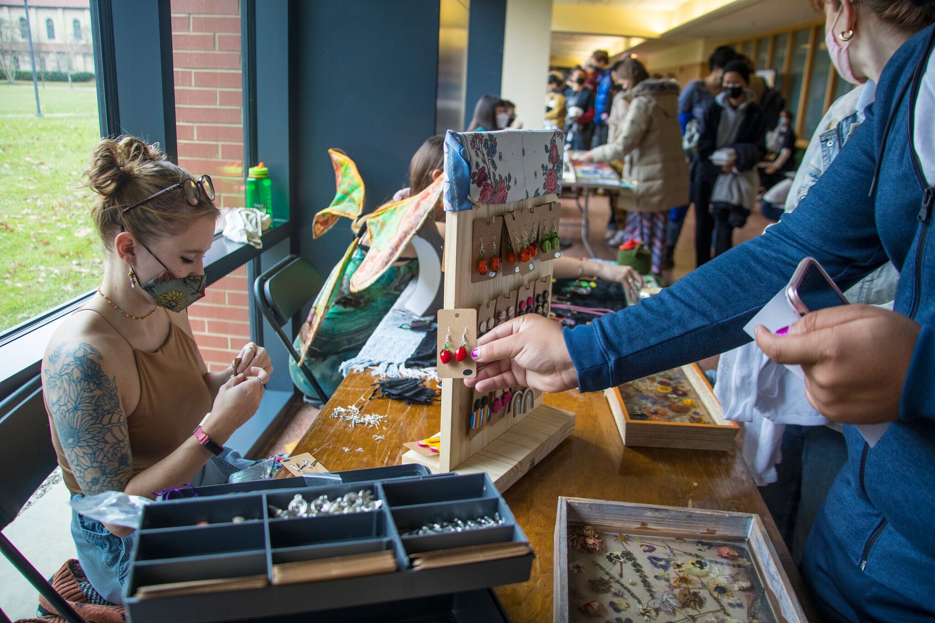 A student makes a pair of earrings at a market.