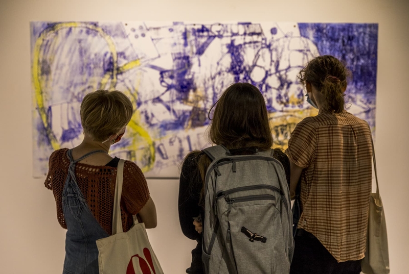 Three students look at a drawing in an art exhibit.