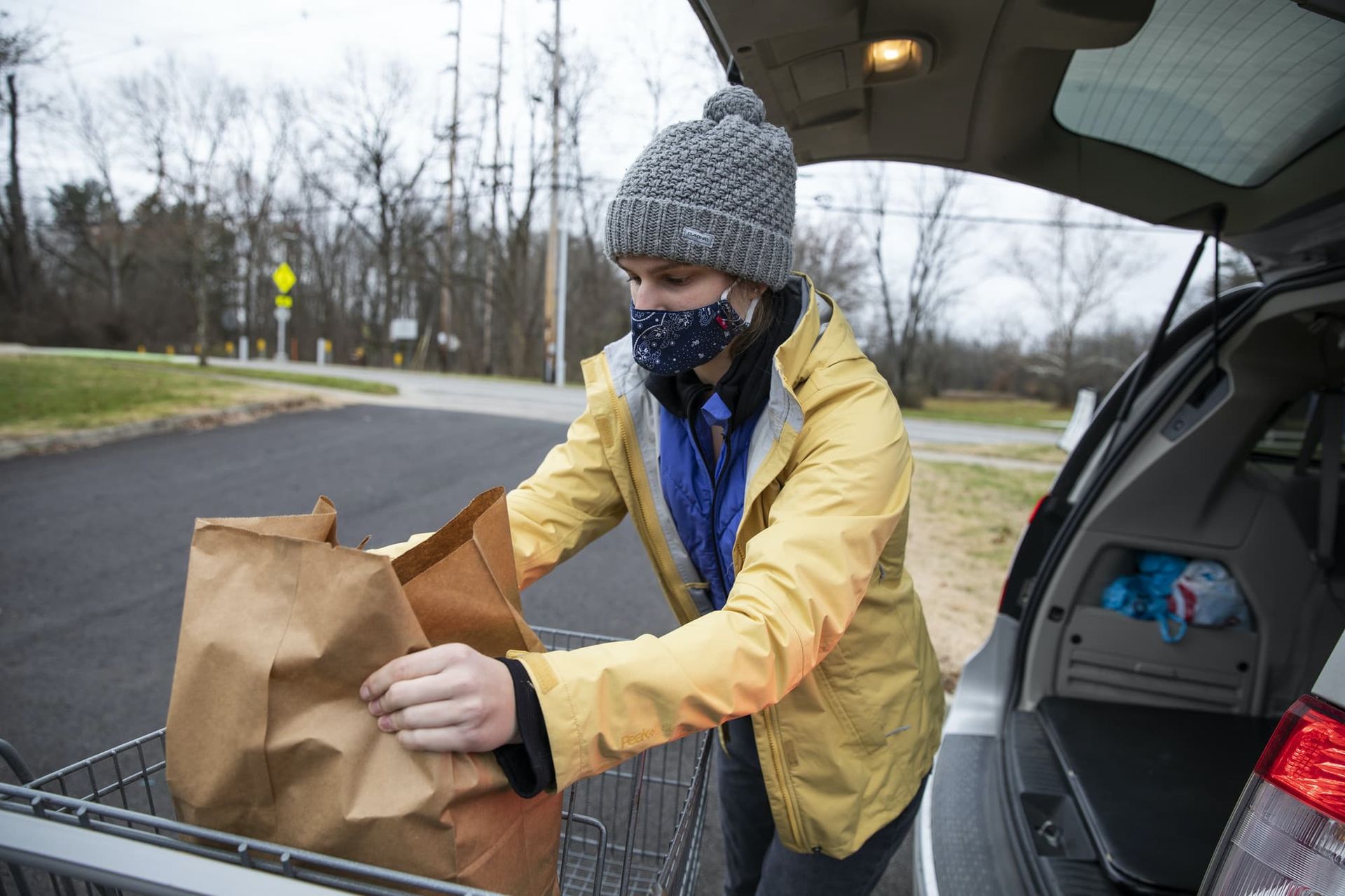 A girl loads groceries into the trunk of a car. 
