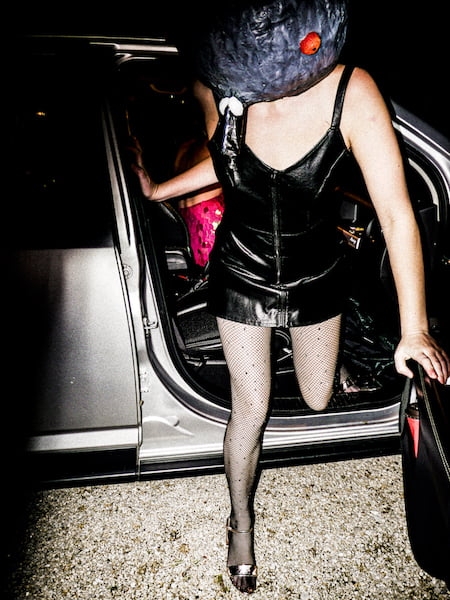 A person coming out of a car wearing black fishnet stockings and matching leather outfit.