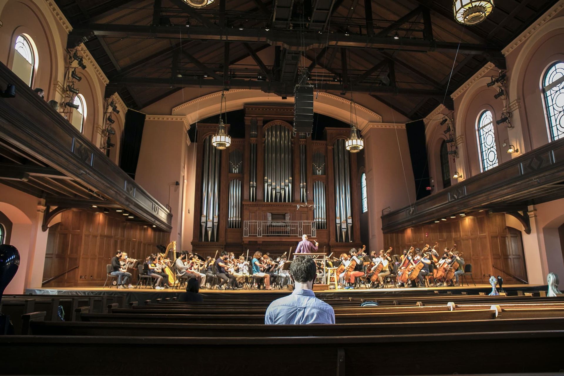 A person sits alone in a concert hall and listens to an orchestra rehears.