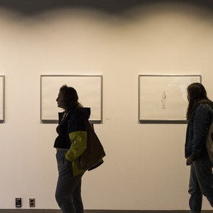 Two students walk by artwork hanging on a wall.