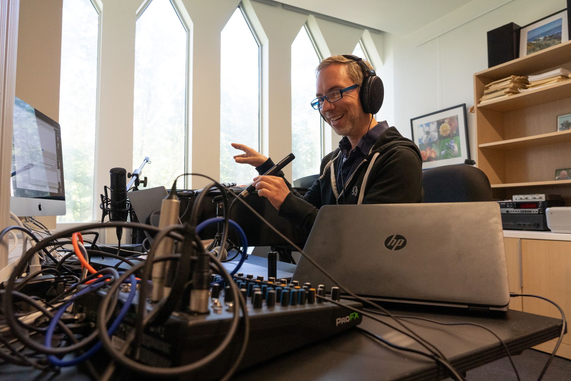 A man wearing headphones speaks into a microphone while seated at his desk.