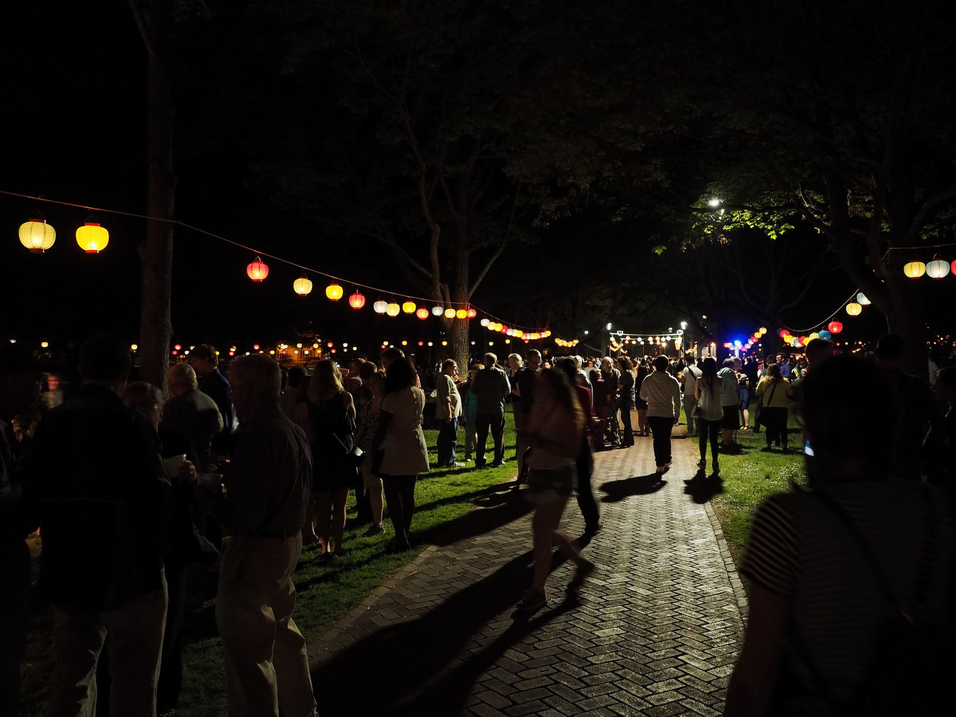 People walk in a park at night with glowing lanterns overhead