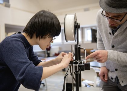 A girl and teacher work on a 3D printer.