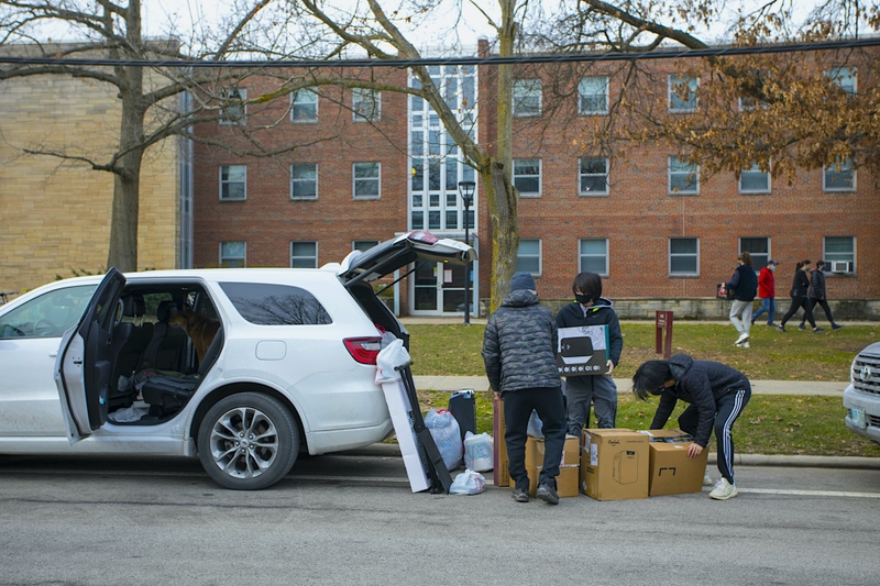 People unload boxes and luggage from the trunk of a car.