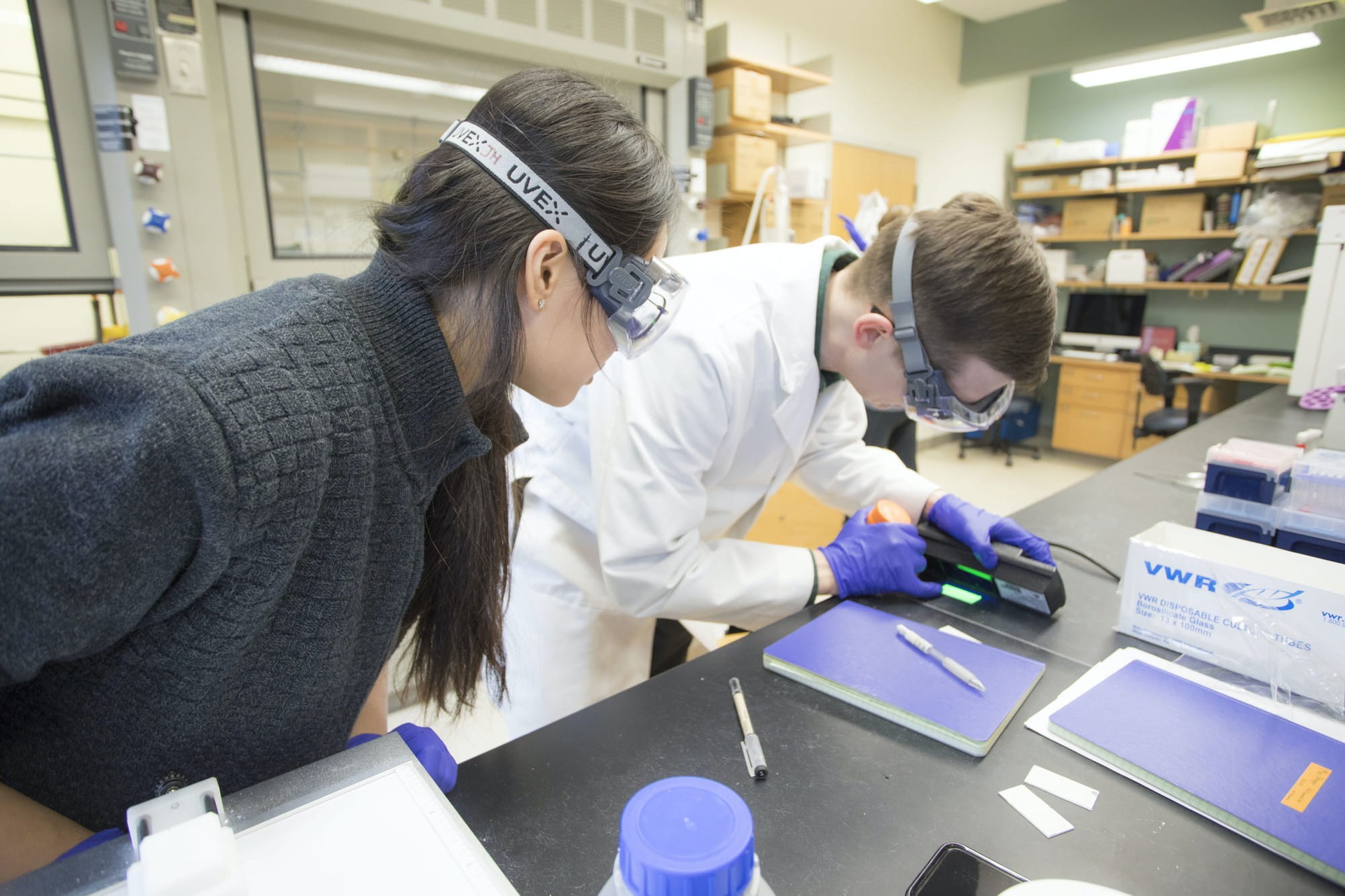 A student and teacher look at a glowing element on a lab table.