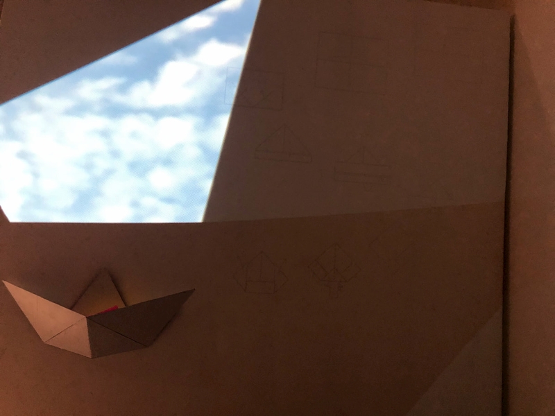 An origami piece is next instructions and a view of clouds.