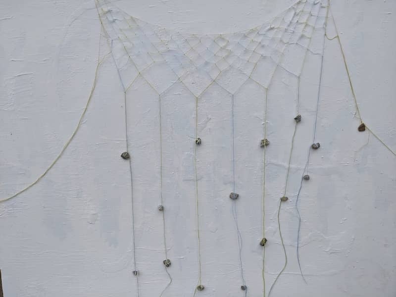 A mesh of thread with rocks tied on long strings at the bottom
