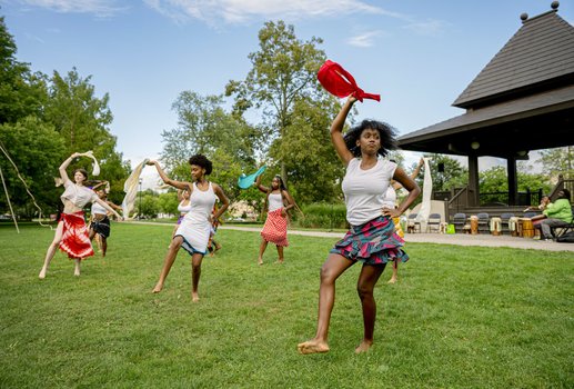 Dancers dance in a grassy park.