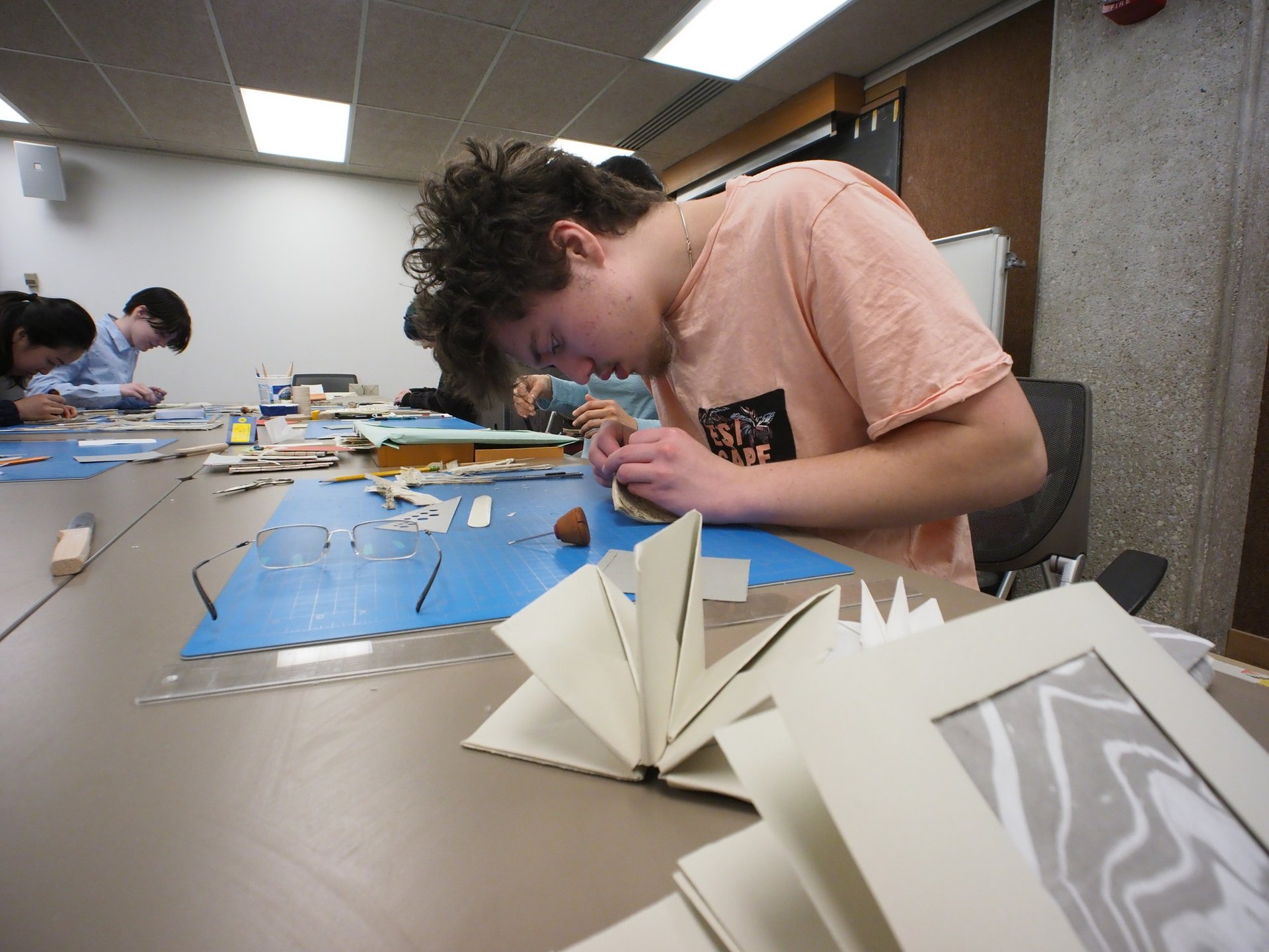 A boy uses instruments to works on a piece of handmade paper.