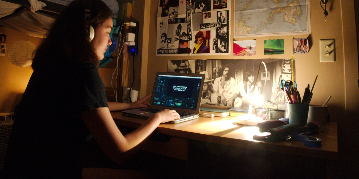 A student works on a laptop with large posters on the wall in front of her.
