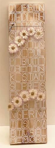 A long wooden plaque with letters and daisys.