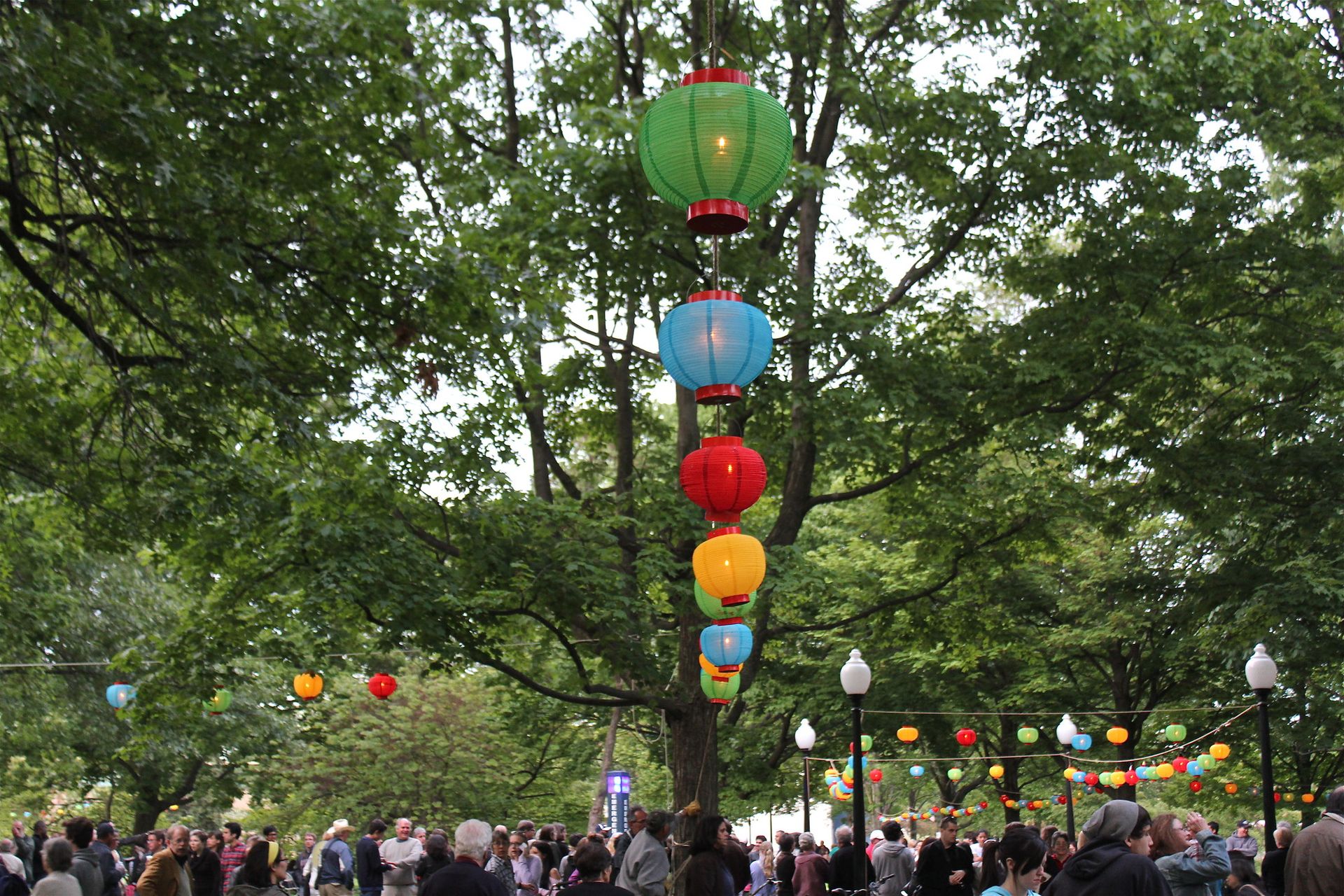 A large group of people stand under lots of hanging lanterns. 