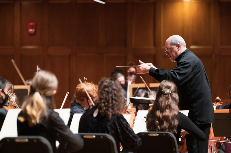 A older male conductor conducts a college orchestra.