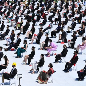 A large graduating class sit 6 feet apart on a football field.