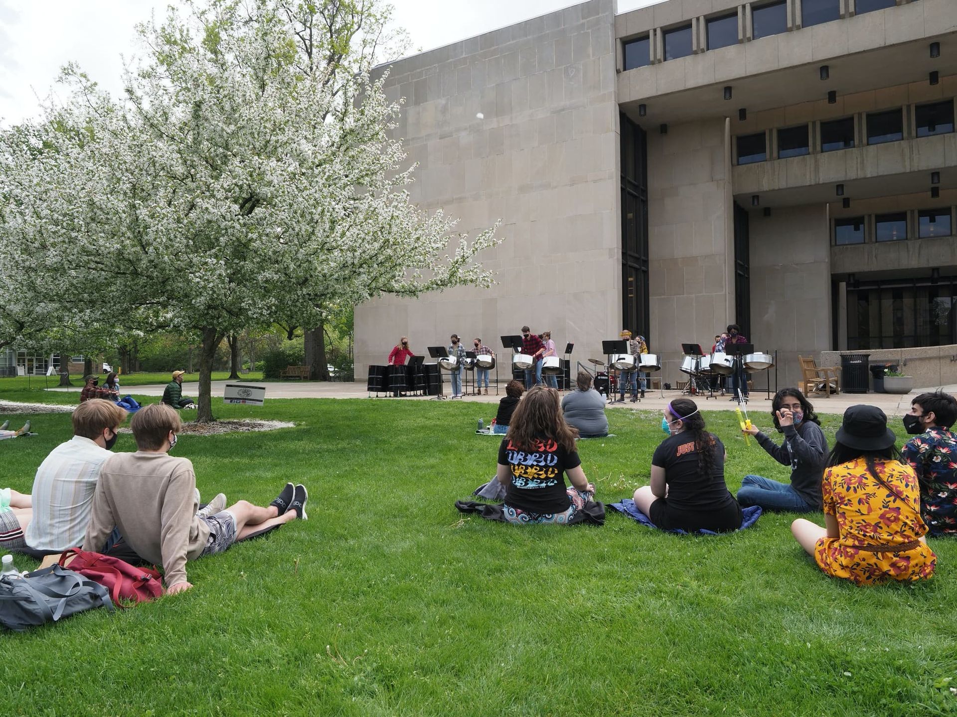 Students sit on the ground and listen to a steel drum band.