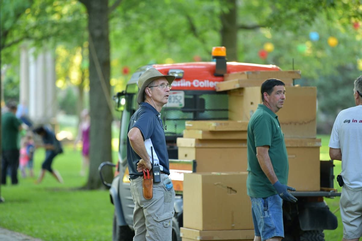 Two men stand next to a club car that has boxes on it.