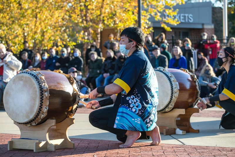 Two taiko drummers play outside and in front of a large audience.