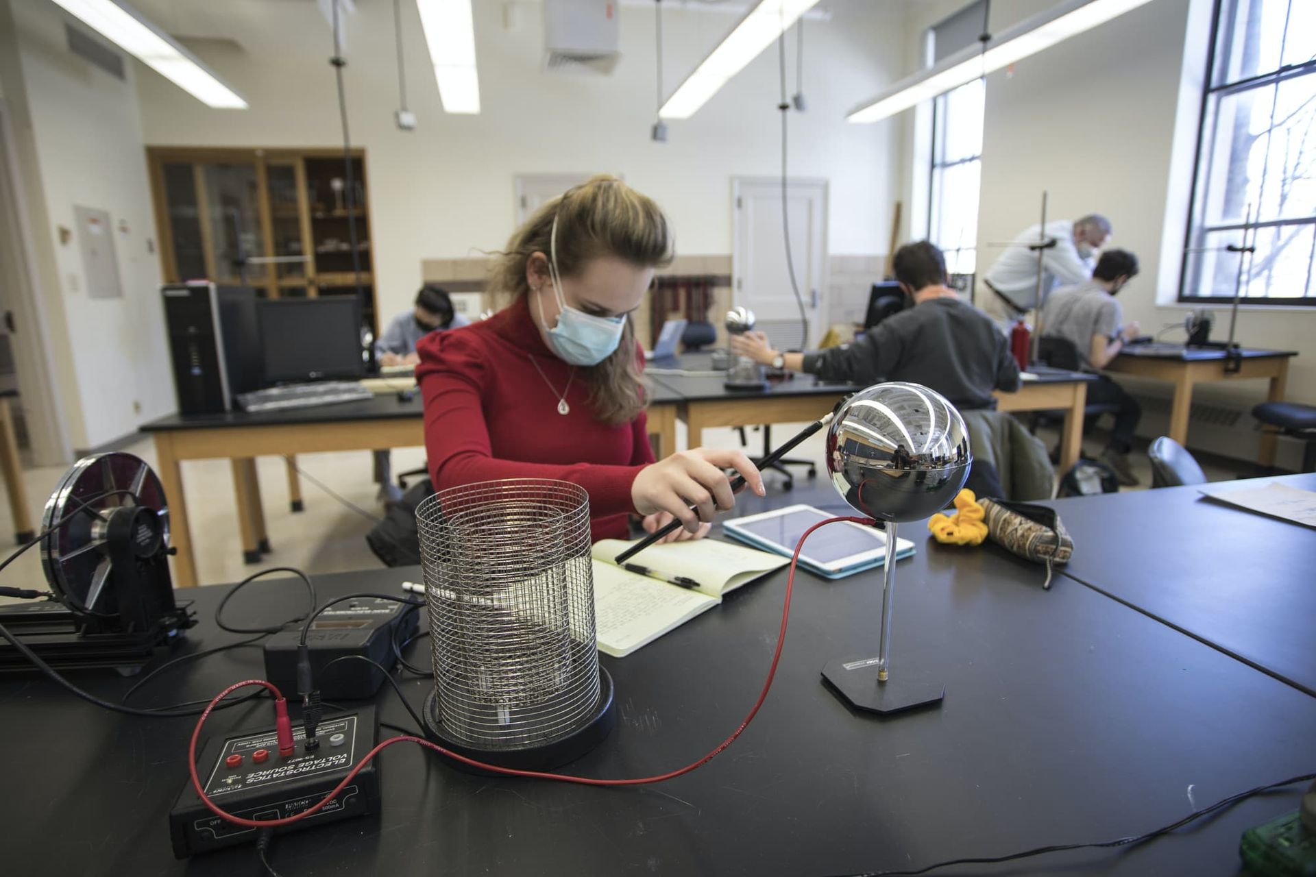 A girl taps a sphere with a metal stick in a physics lab.