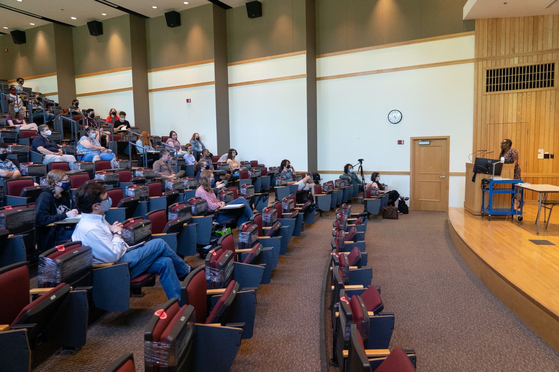 A woman at a podium speaks to an audience in a large lecture hall.