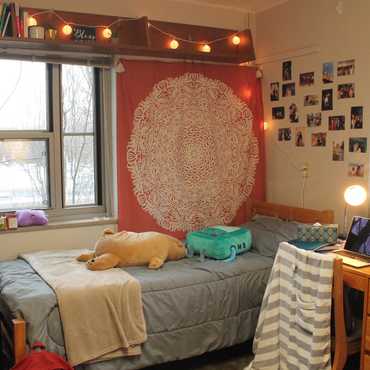 Tapestry, large string lights, and photos hang aover a student's bed.