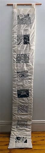 A long hand quilted banner hanging from a wooden stick.