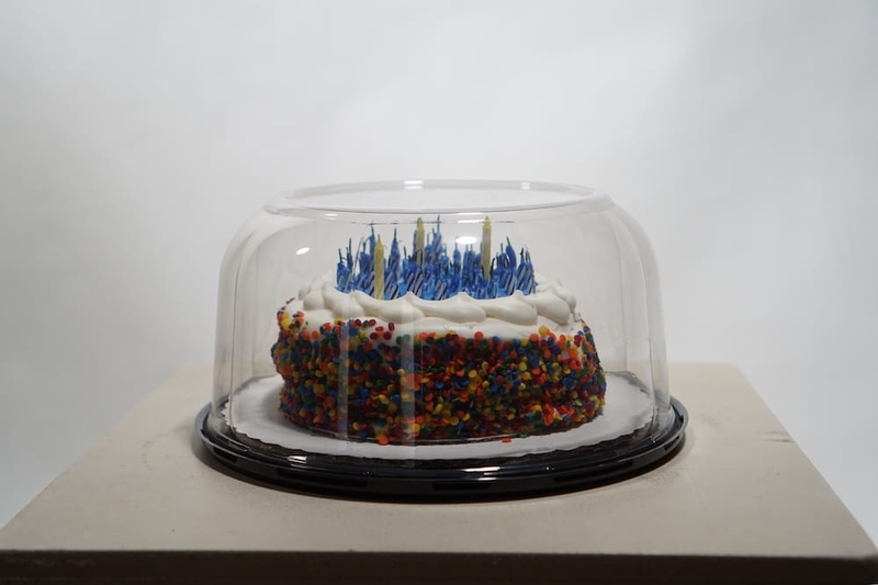 A birthday cake with candles in a plastic carry-out container